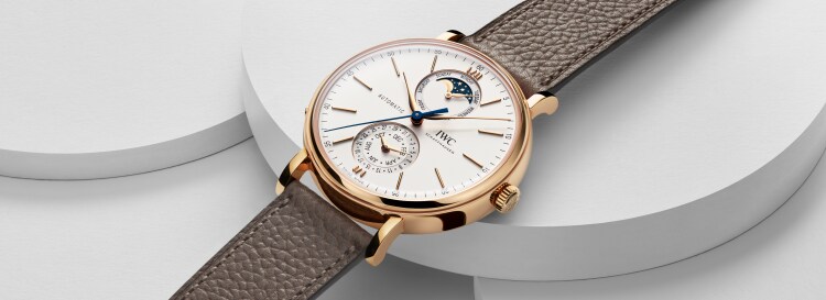 Image of IWC Portofino Complete Calendar IW359002 with white dial, gold case and taupe calfskin strap placed on a white surface.